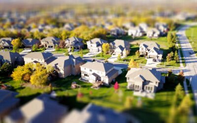Photographie aérienne en mode tilt-shift d'un quartier de banlieue avec des pelouses vertes et des routes.