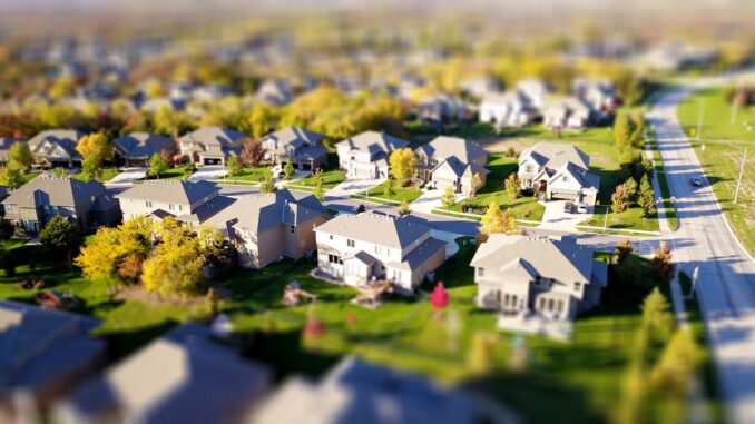 Photographie aérienne en mode tilt-shift d'un quartier de banlieue avec des pelouses vertes et des routes.