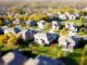 Photographie aérienne en mode tilt-shift d'un quartier de banlieue avec des pelouses vertes et des routes.