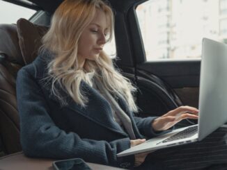 Femme d'affaires travaillant à distance sur un ordinateur portable, assise à l'arrière d'une voiture de luxe. Élégante, moderne et concentrée.