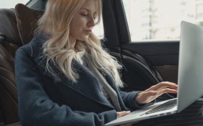 Femme d'affaires travaillant à distance sur un ordinateur portable, assise à l'arrière d'une voiture de luxe. Élégante, moderne et concentrée.
