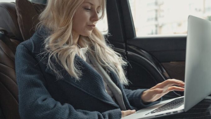 Femme d'affaires travaillant à distance sur un ordinateur portable, assise à l'arrière d'une voiture de luxe. Élégante, moderne et concentrée.